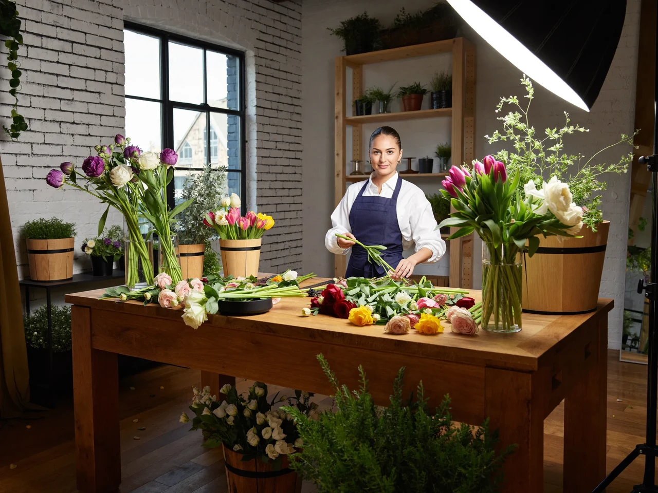 Lyst blomsterværksted med træbord, spande med stilke og morgenlys